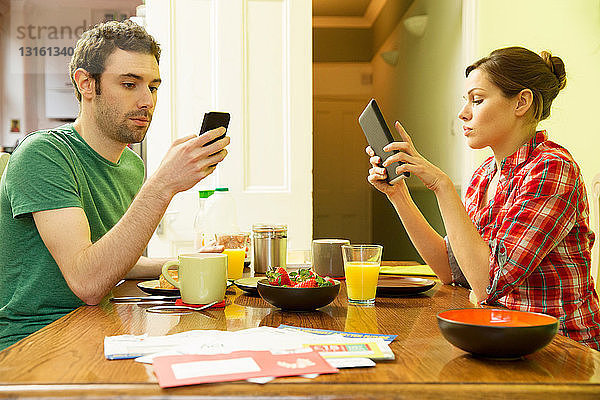 Mann mit Smartphone und Frau mit digitalem Tablet beim Frühstück