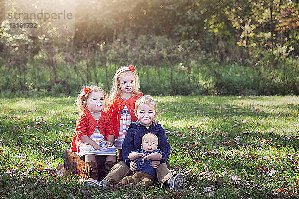 Vier Kinder einer Familie auf mit Herbstlaub bedecktem Gras posieren lächelnd für ein Foto