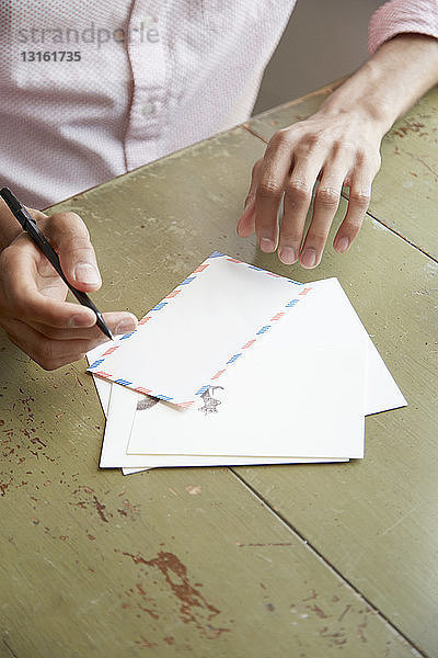 Schrägansicht auf die Hände eines jungen Mannes beim Schreiben eines Luftpostbriefes