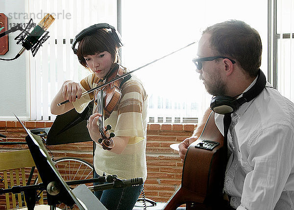 Junger Mann und Frau spielen Geige und Gitarre in Musikraumprobe