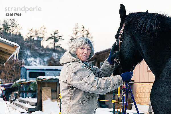 Ältere erwachsene Frau steht mit Pferd in verschneiter Landschaft