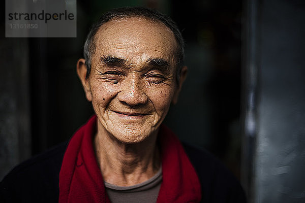 Porträt eines älteren Mannes mit rotem Schal um den Hals  der lächelnd in die Kamera blickt