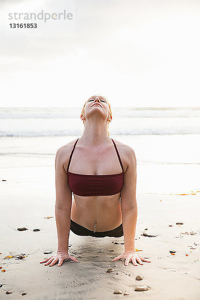 Mittlere erwachsene Frau  die eine Planken-Yoga-Pose am Strand praktiziert