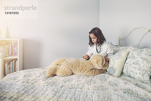 Im Laborkittel gekleidetes Mädchen im Bett sitzend mit Stethoskop auf Plüschtier