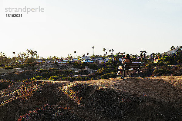 Rückansicht einer jungen Frau  die auf einer Klippenbank sitzt  fotografiert Ansicht auf einem Smartphone  San Clemente  Kalifornien  USA