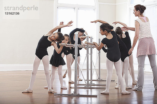 Ballettlehrerin unterrichtet Gruppe von Mädchen Ballettposition an der Stange