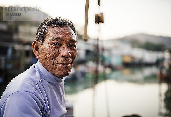 Porträt eines älteren Mannes  Seitenansicht  vor Booten auf dem Wasser  in die Kamera blickend