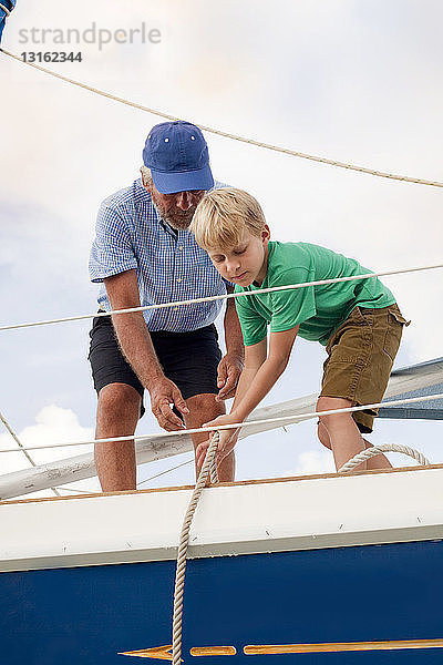 Junge hilft Großvater beim Ziehen von Seilen auf Segelboot