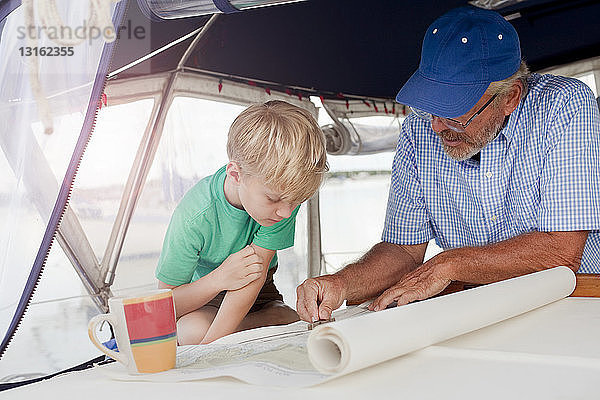 Junge und Grossvater planen auf Navigationskarten in der Segelbootkabine