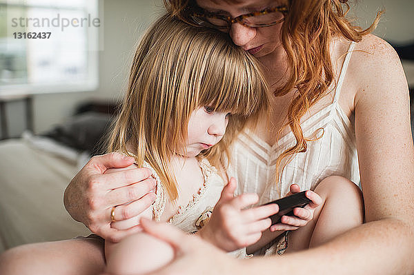 Mutter umarmt Tochter  benutzt Smartphone
