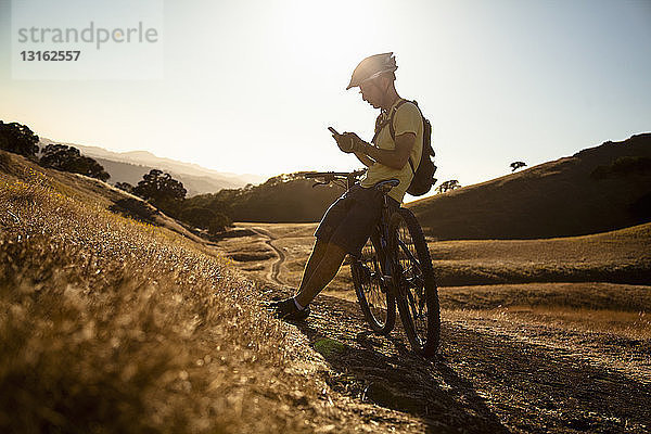 Silhouettierter junger männlicher Mountainbiker mit Smartphone  Mount Diablo  Bay Area  Kalifornien  USA