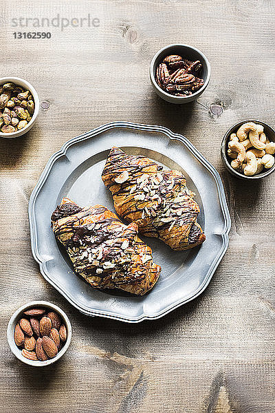 Draufsicht auf Croissant auf Serviertablett mit Auswahl von Nüssen in Schalen