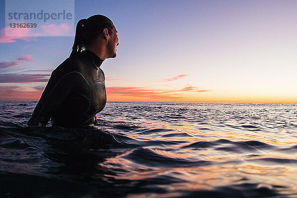 Weibliche Surferin watet bei Sonnenuntergang im Meer  Cardiff-By-The-Sea  Kalifornien  USA