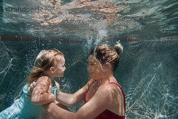 Unterwasseraufnahme einer Mutter  die ihre Tochter hält und ihr beim Schwimmenlernen hilft