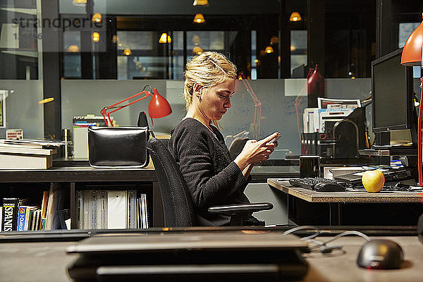 Weibliche Büroangestellte am Schreibtisch mit Mobiltelefon