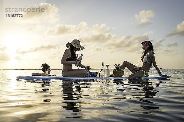 Zwei junge Frauen bereiten bei Sonnenuntergang auf dem Paddelbrett Cocktails zu  Islamorada  Florida  USA