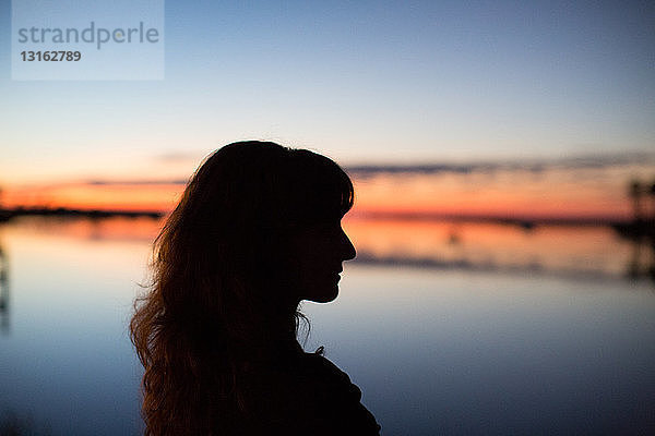 Seitenansicht einer jungen Frau in Silhouette mit Blick auf das Wasser