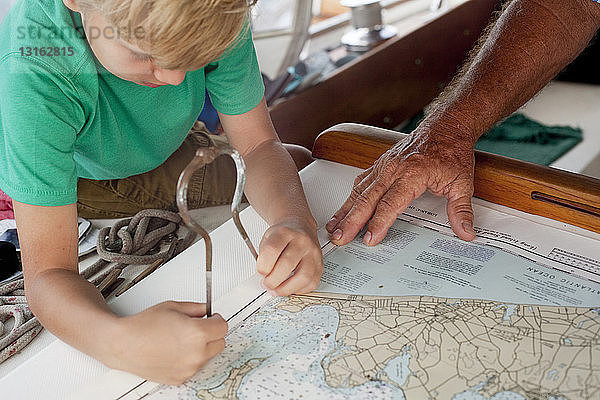 Junge und Großvater benutzen Trennlinien auf Navigationskarten in der Segelbootkabine
