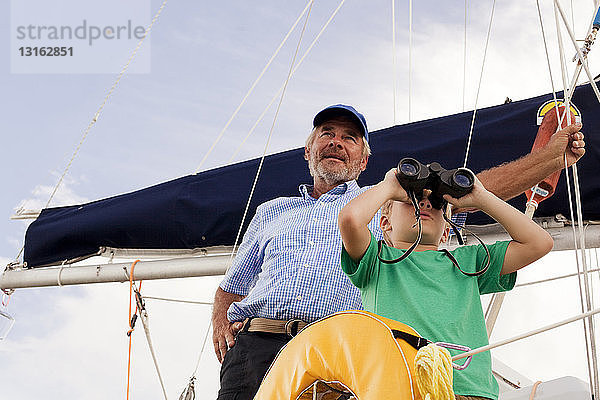 Junge und Großvater auf einem Segelboot beim Blick durch ein Fernglas