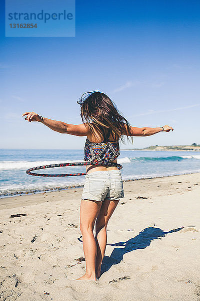 Frau mit Hula-Hoop-Reifen am Strand  Rückansicht