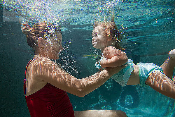 Unterwasseraufnahme einer Mutter  die ihre Tochter hält und ihr beim Schwimmenlernen hilft