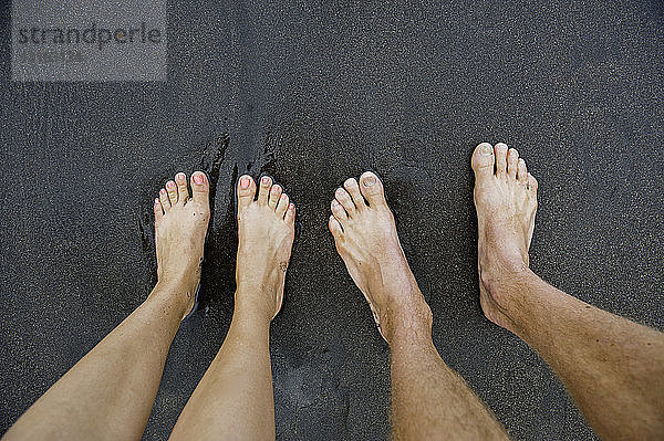 Paare männlicher und weiblicher Füße auf schwarzem Sand