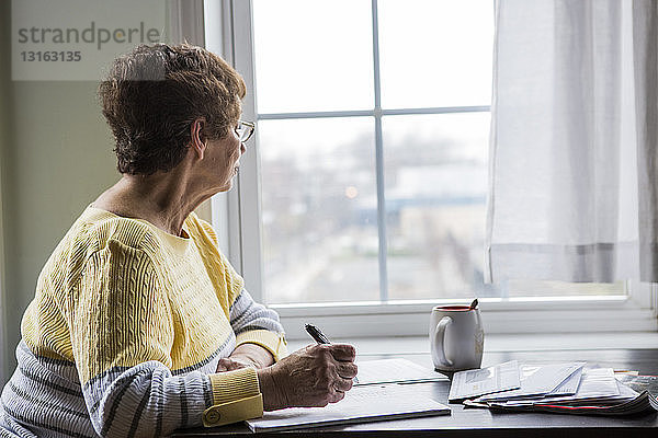 Ältere Frau denkt am Schreibtisch