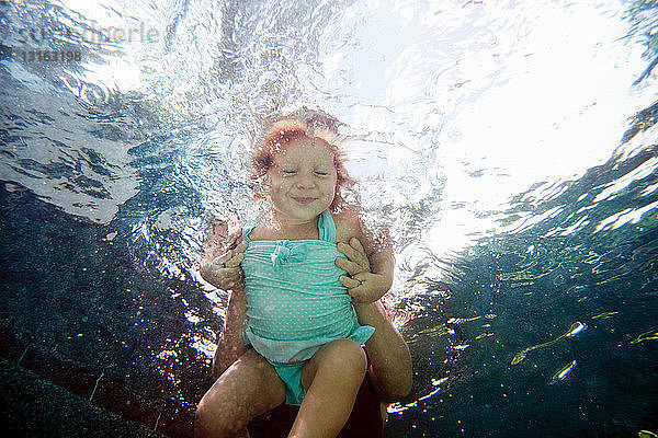 Unterwasserporträt eines Mädchens  das schwimmen lernt und vor der Kamera lächelt
