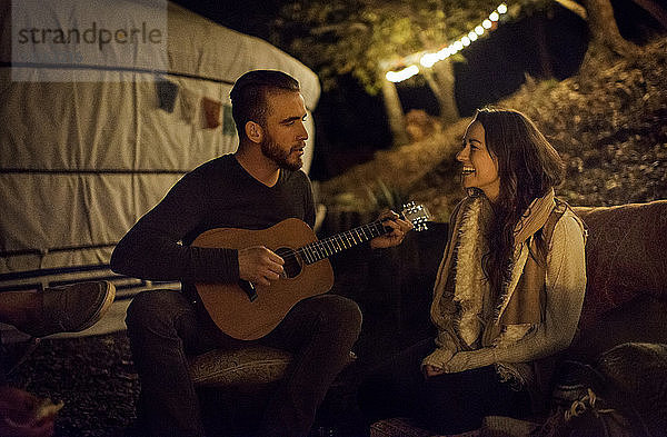 Junger Mann bringt einer jungen Frau mit Gitarre neben der Jurte ein Ständchen