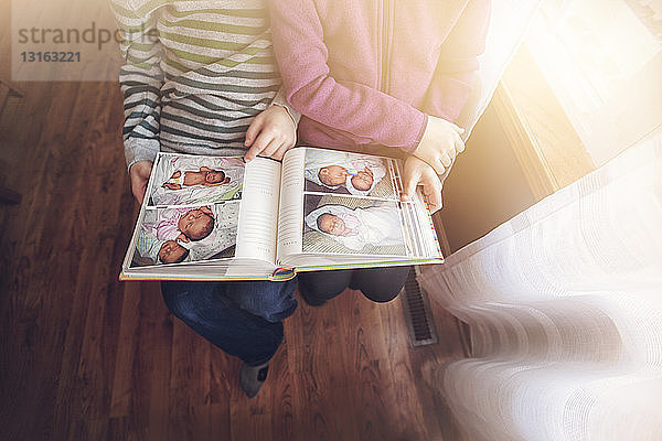 Nackenansicht von Zwillingsjungen und -mädchen  die Fotoalben von sich selbst als Babys betrachten