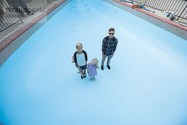 Hochwinkelaufnahme von Geschwistern  die in einem leeren Schwimmbad stehen und zur Kamera aufschauen
