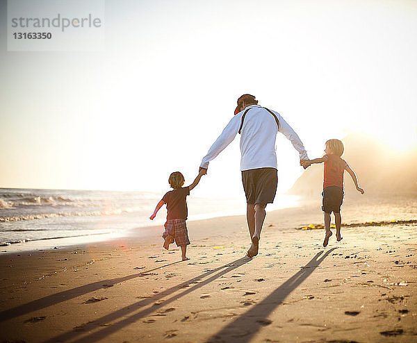 Vater und Söhne gehen bei Sonnenuntergang Hand in Hand am Strand