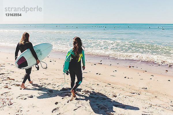Paar mit Surfbrettern in der Hand  auf das Meer hinausgehend  Rückansicht