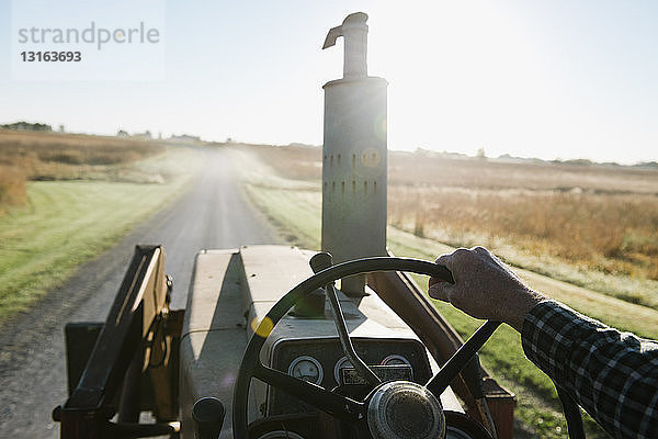 Über-Schulter-Ansicht eines älteren männlichen Landwirts  der einen Traktor auf einer Landstraße fährt  Plattsburg  Missouri  USA
