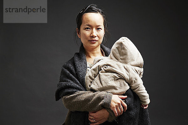 Studioporträt einer mittleren erwachsenen Frau  die einen kleinen Sohn hält