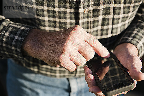 Nahaufnahme eines älteren männlichen Landwirts mit Touchscreen auf einem Smartphone