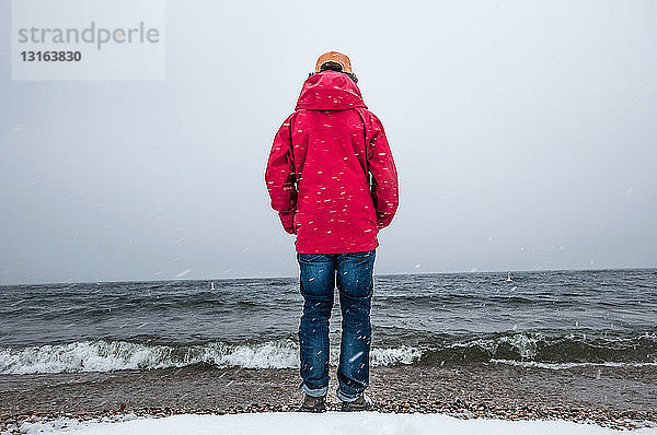 Rückansicht eines jungen Mannes in rotem Mantel in voller Länge mit Blick auf den Ozean