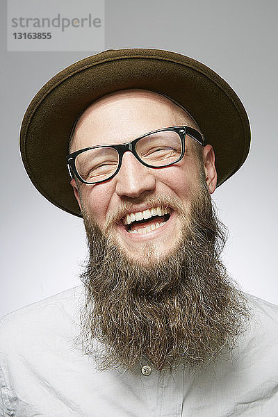Studioporträt eines lachenden erwachsenen Mannes in Trilby mit übergroßem Bart
