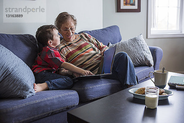 Ältere Frau erklärt ihrem Enkel das Buch  während sie auf dem Sofa liest