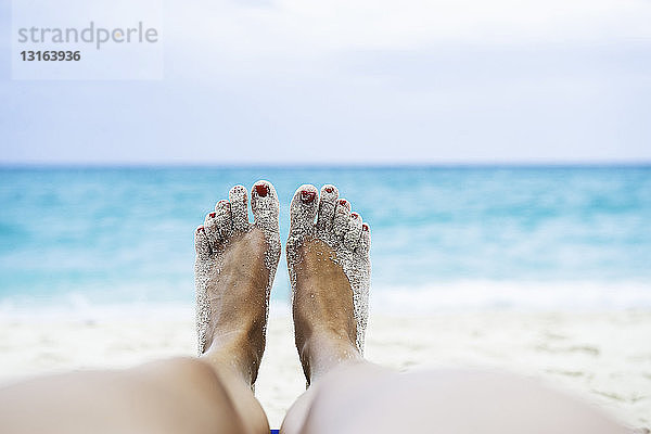 Nahaufnahme der weiblichen Beine und Füße beim Sonnenbaden am Strand