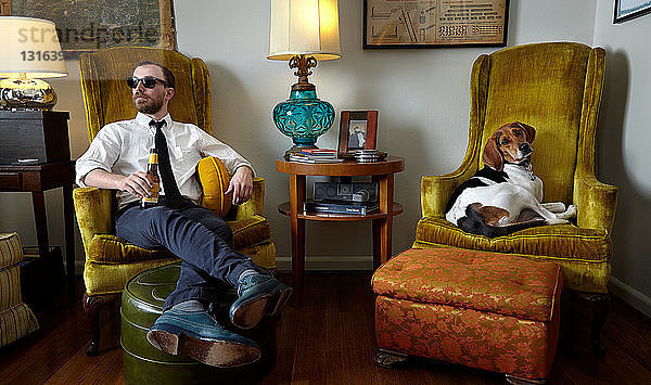 Junger Mann und Haushund entspannen sich im Sessel im Wohnzimmer