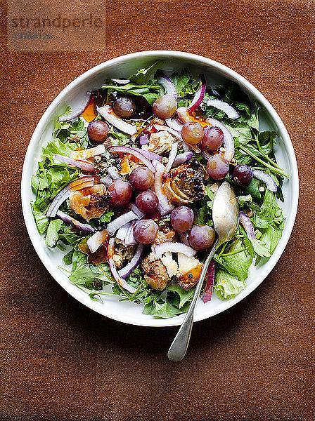 Schale mit gemischtem Salat mit roten Zwiebeln und schwarzen Trauben