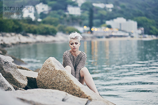 Junge Frau sitzt allein auf Hafenfelsen
