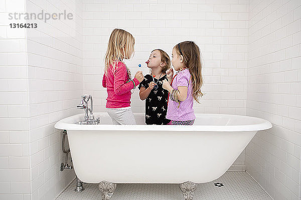 Drei junge Mädchen stehen mit Lutschern in der Badewanne