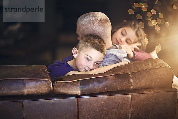 Reifer Mann entspannt sich auf Sofa und umarmt Sohn und Tochter