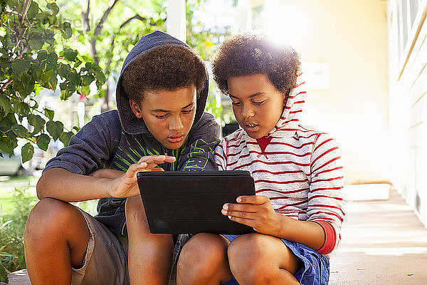 Zwei Brüder benutzen Touchscreen auf digitalem Tablet im Garten