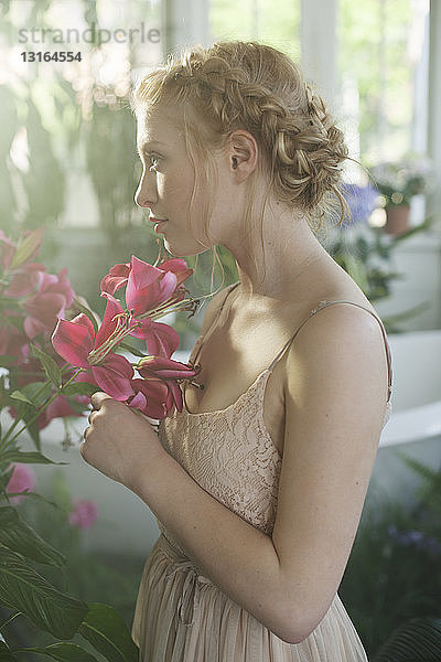 Porträt einer jungen Frau  blondes geflochtenes Haar  riechende rosa Blumen