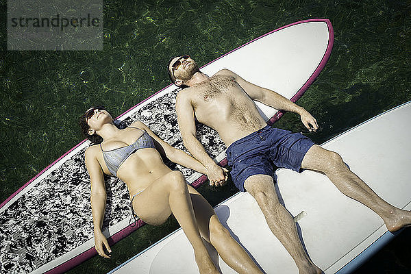 Draufsicht auf ein junges Paar beim Sonnenbaden auf Paddelbrettern