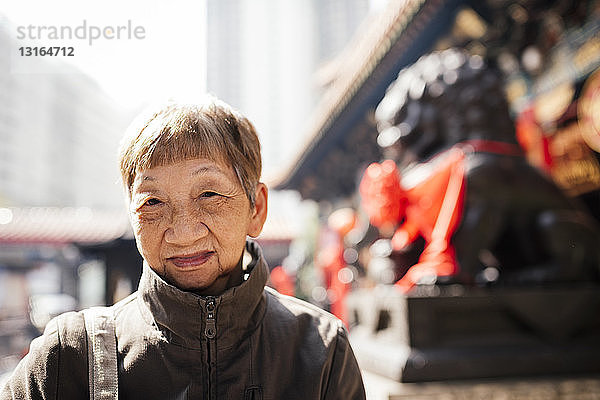 Porträt einer älteren Frau im Mantel vor der Löwenstatue  die in die Kamera schaut