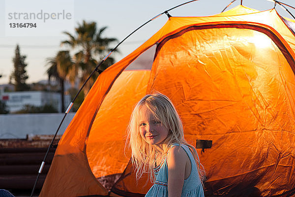 Seitenansicht des Mädchens neben dem orangefarbenen Zelt  lächelnd in die Kamera blickend